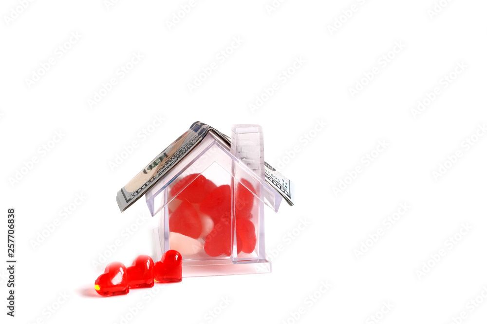 The house from plexiglas. Inside is filled with hearts. Next to the house of the heart. On the roof are dollars. Financing construction concept. House for a family concept. Copy space. The house from plexiglas. Inside is filled with hearts. Next to the house of the heart. On the roof are dollars. Financing construction concept. House for a family concept. Copy space.