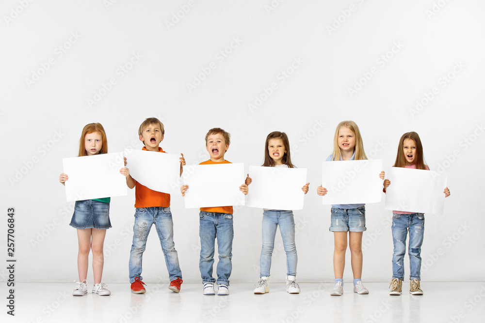 Obraz premium Group of angry screaming children with a white empty banners isolated in white studio background. Education and advertising concept. Protest and children's rights concepts.