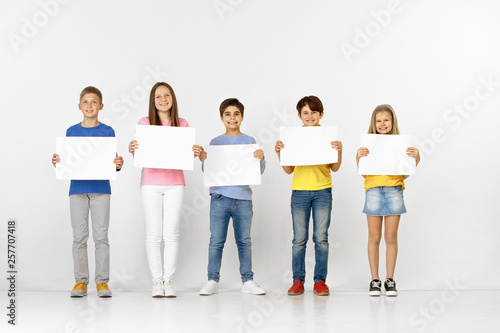 Group of happy smiling children with a white empty banners isolated in white studio background. Education and advertising concept