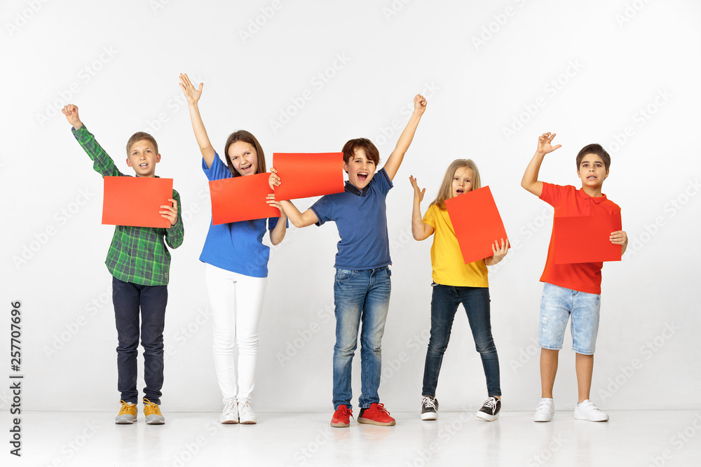 Group of happy smiling children with red empty banners isolated in white studio background. Education and advertising concept Group of happy smiling children with red empty banners isolated in white studio background. Education and advertising concept