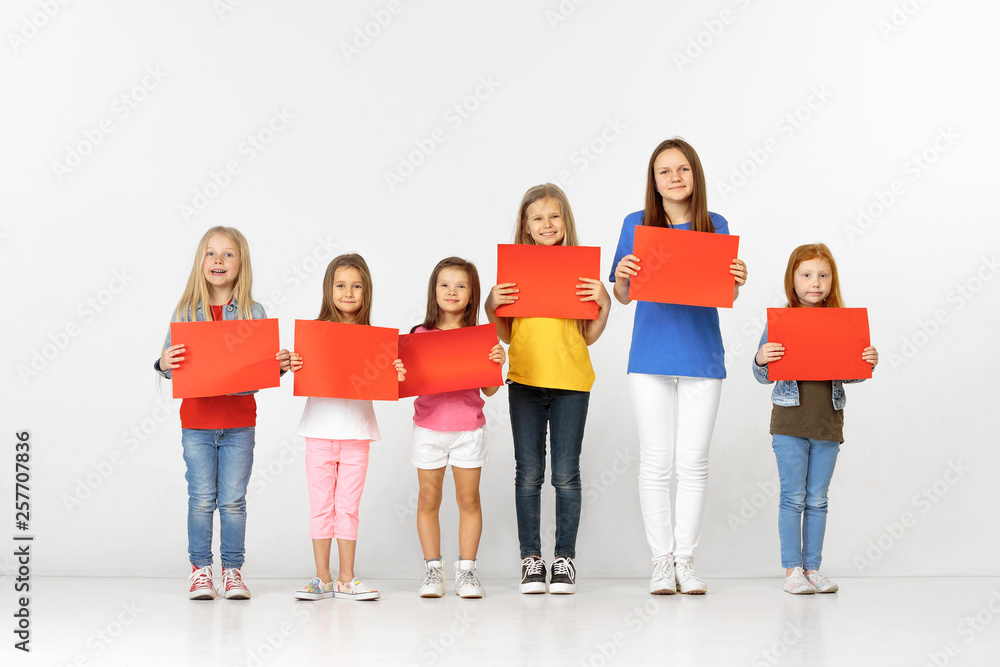 Obraz premium Group of happy smiling children with red empty banners isolated in white studio background. Education and advertising concept