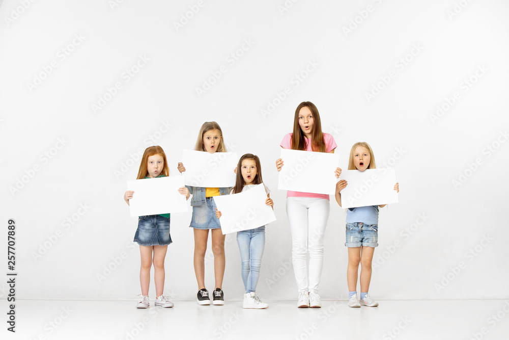 Group of happy surprised children with a white empty banners isolated in light studio background. Education and advertising concept Group of happy surprised children with a white empty banners isolated in light studio background. Education and advertising concept