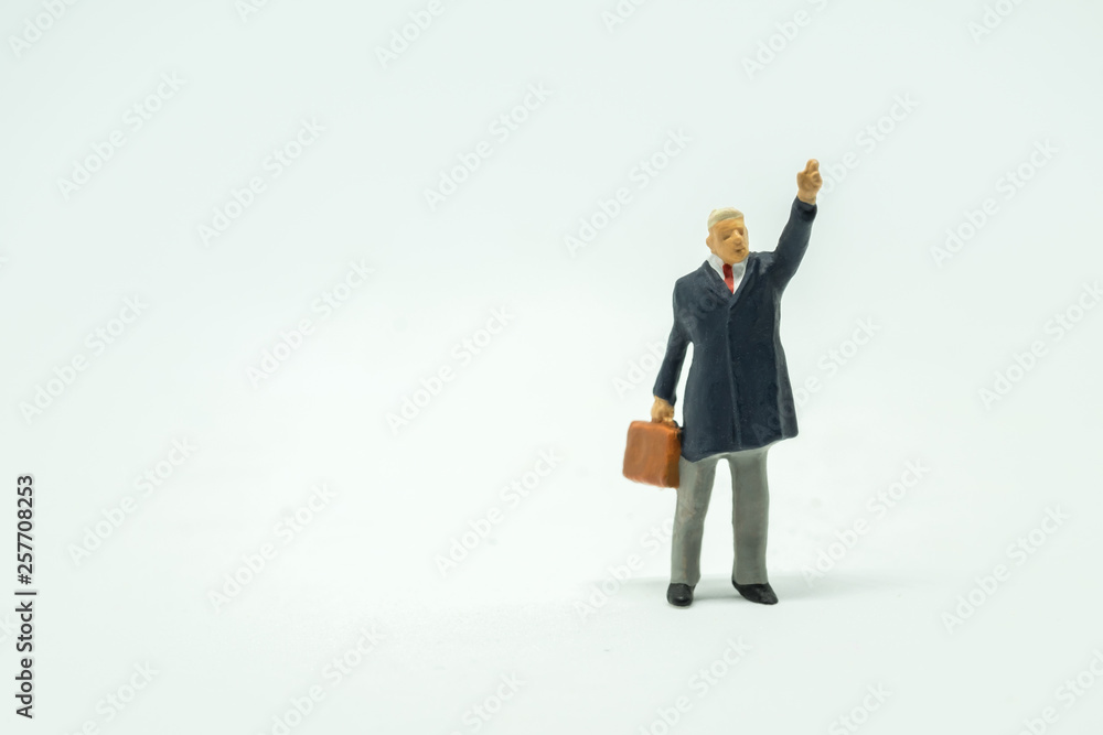 Business and Travel Concept. Close up of businessman miniature figure standing and rise hand up to call something on white background with hand bag briefcase. Business and Travel Concept. Close up of businessman miniature figure standing and rise hand up to call something on white background with hand bag briefcase.