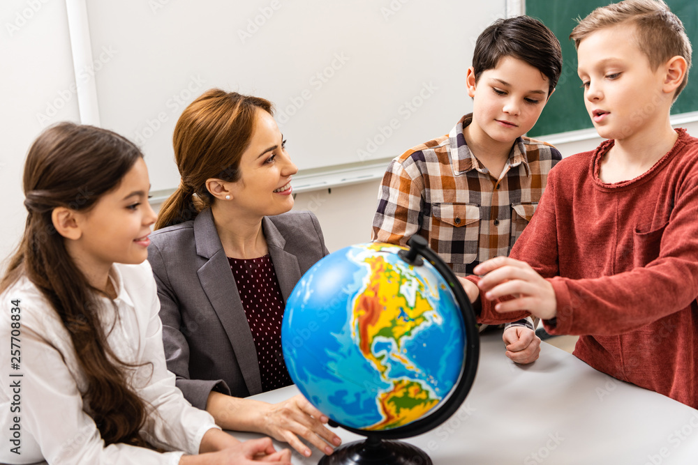 Teacher and pupils looking at globe while studying geography in classroom Teacher and pupils looking at globe while studying geography in classroom
