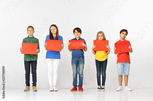 Group of sad serious children with red empty banners isolated on white studio background. Education and advertising concept