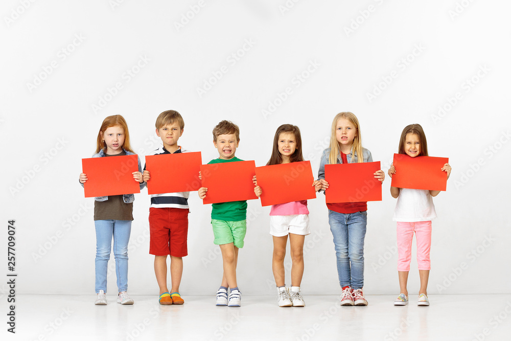 Group of unhappy angry children with red empty banners isolated in white studio background. Education and advertising concept. Protest and children's rights concepts.