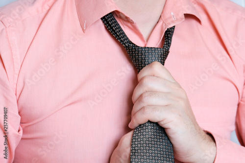 A man in a pink shirt straightens a tie, a man in a tie, the morning of the groom, the groom's fees, the groom in a shirt. Businessman in troubles concept.