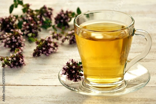 A сup of fragrant tea with fresh oregano on the white wooden table.