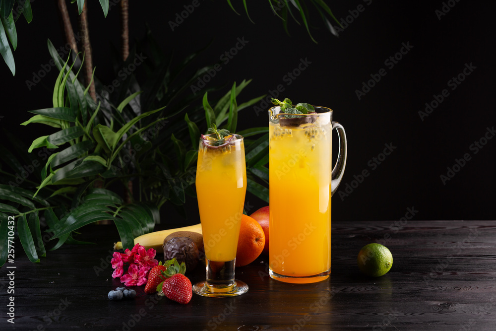Fototapeta premium Mango lemonade - passion fruit in a jug and a glass and fruit on a dark wooden background