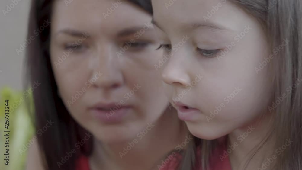 Portrait of a little cute pretty girl playing educational game close up. Her mother is helping the child, advising her, face is blurred. Concept of kids growing Portrait of a little cute pretty girl playing educational game close up. Her mother is helping the child, advising her, face is blurred. Concept of kids growing