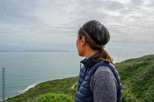 Young sporty Asian woman looking out at the beautiful ocean view. Young woman hiker standing admiring the view. healthy active lifestyle concept photo