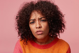 Close up portrait of african american female with afro hairstyle looking with suspicion peers gaze, examine something, squint, isolated over pink background