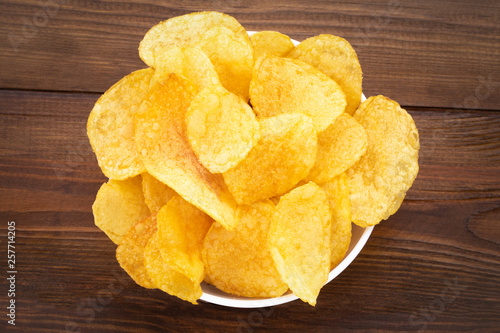 Crispy potato chips in bowl on wooden background, top view