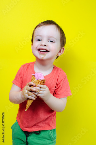 Laughing boy eating ice cream cones  stay along background of bright colored wall, have summer mood and laugh