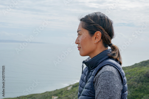 Young sporty Asian woman looking out at the beautiful ocean view. Young woman hiker standing admiring the view. healthy active lifestyle concept photo