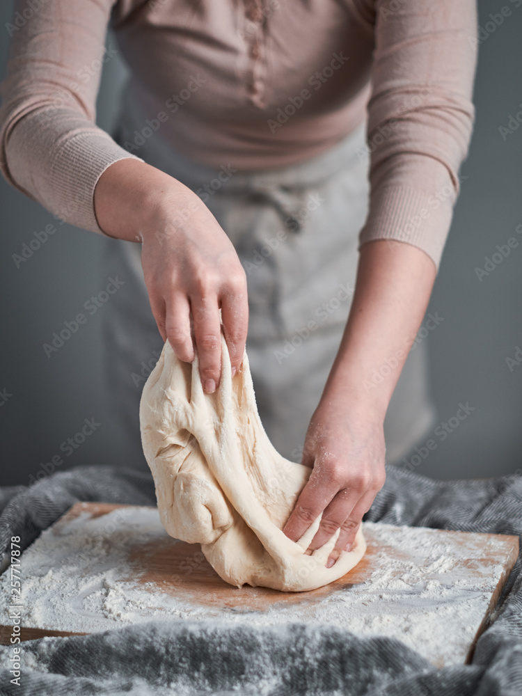 Woman hands kneading a bread dough on a wooden board