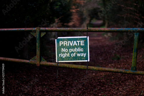 Private no right of way sign on old rusty metal gate blocking access to woodland countryside track with shallow depth of field
