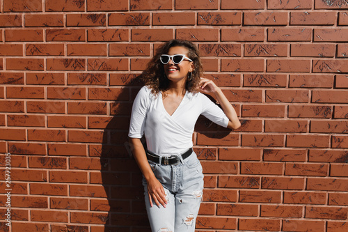 Attarctive elegant young woman hipster in a white sunglasses in a summer denim pants and white t-shirt