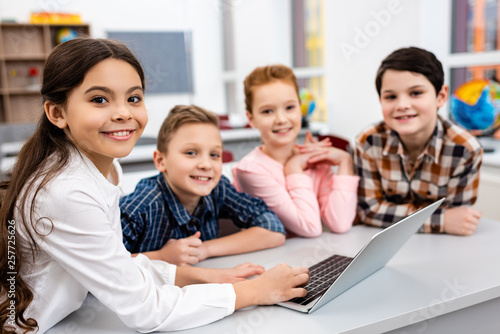 Obraz na plátne Happy preteen pupils using laptop in classroom with smile