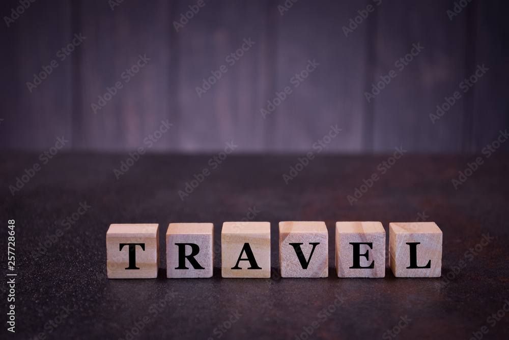 Obraz premium The word travel on wooden cubes, on a dark background, symbols signs