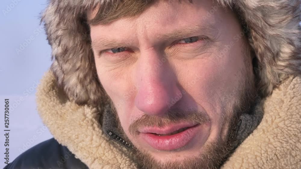Close-up shot of middle-aged explorer in hood and coat freezing and trembling in cold and watching seriously into camera. Close-up shot of middle-aged explorer in hood and coat freezing and trembling in cold and watching seriously into camera.