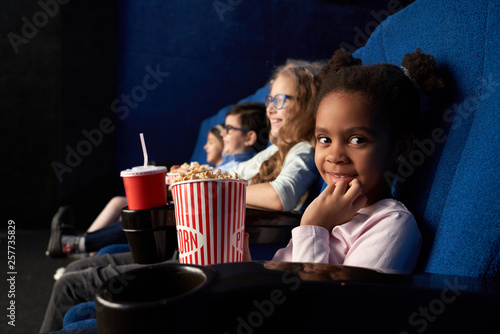 Cuadro en lienzo Cute girl sitting in cinema with friends, looking at camera.