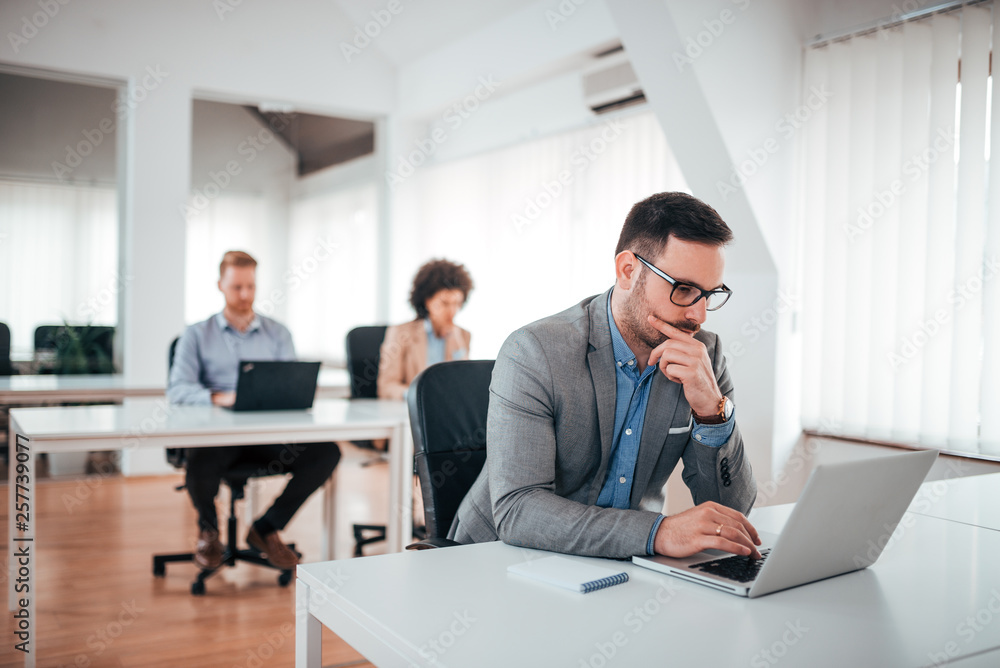 Handsome pensive businessman working on laptop in coworking office. Handsome pensive businessman working on laptop in coworking office.