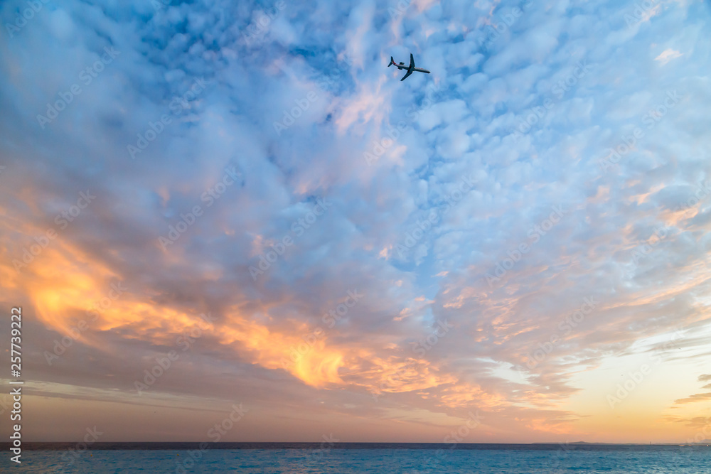Airplane flying in the cloudy sunset sky over the sea. Travel transport airline sky background concept. Copy space.