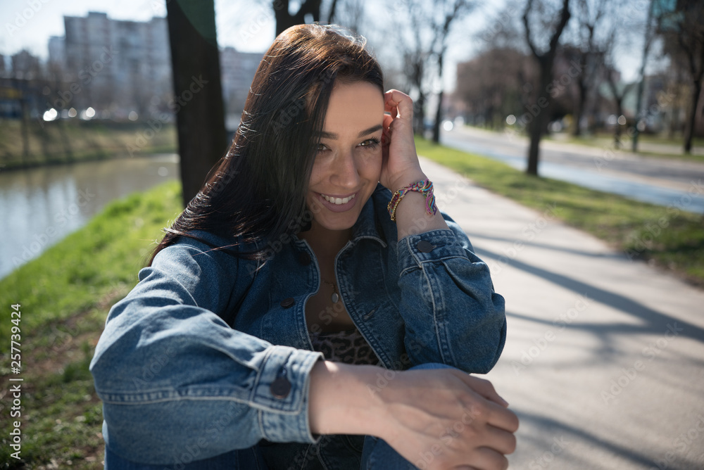 beautiful young woman in denim jacket smiling while sitting in park beautiful young woman in denim jacket smiling while sitting in park