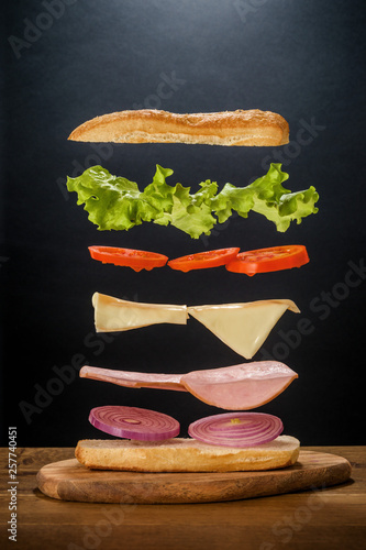 Hovering components of delicious andwich on the black background and wooden oak table. photo