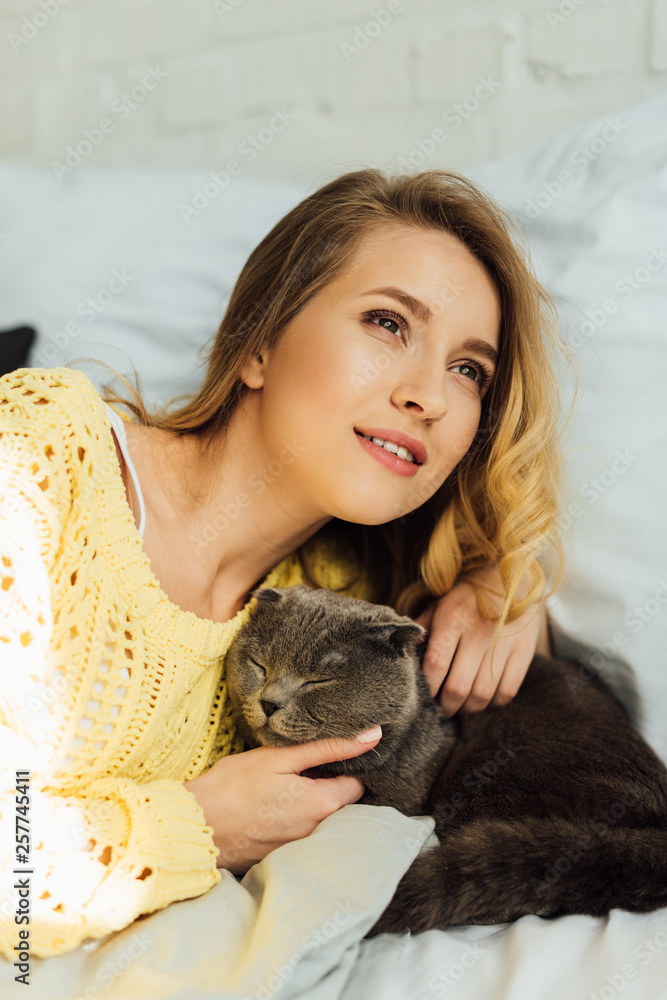 beautiful smiling girl in knitted sweater lying in bed and hugging scottish fold cat beautiful smiling girl in knitted sweater lying in bed and hugging scottish fold cat