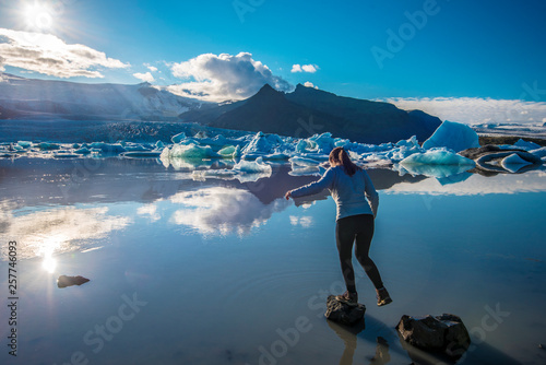 Girl teenager jumping over rocks in the border of Fjallsarlon glacier lake facing to the sun. Southern Iceland, Vatnajokull national park. photo