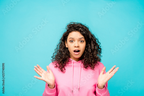 shocked curly african american girl looking at camera isolated on blue