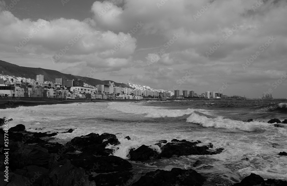 Rocky coast with rough sea, city and cloudy sky, Las Palmas de Gran Canaria, black and white effect, Canary Islands