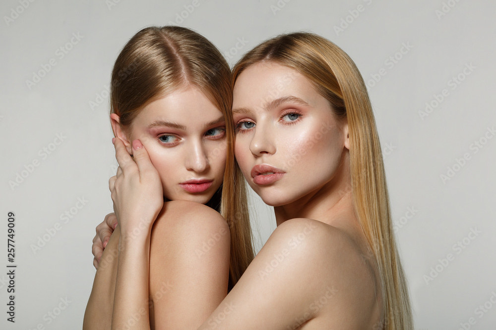 Young beautiful faces of two adult girls with bare shoulders on grey background Young beautiful faces of two adult girls with bare shoulders on grey background