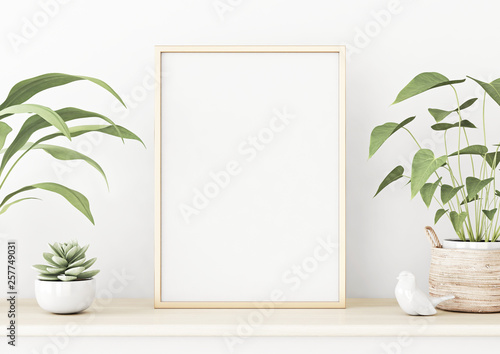 Vertical poster mockup with golden metal frame standing on wooden table and decorated with succulent and green plants in basket on empty white wall background. 3D rendering, illustration. © marina_dikh