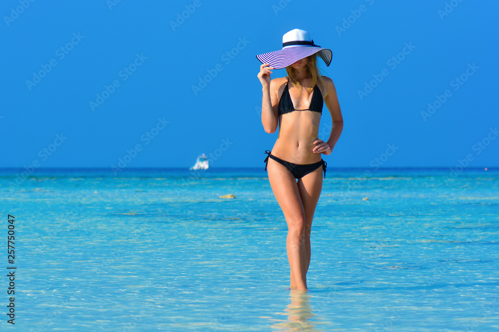 Fit girl on a tropical beach with hat. Sexy black bikini body woman on  paradise tropical
