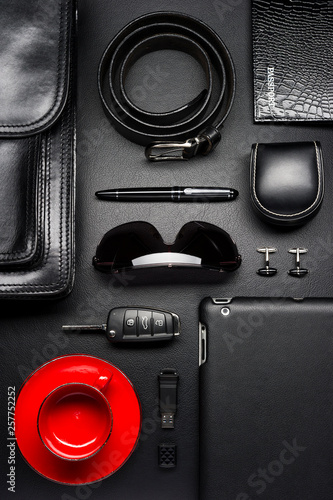 Man accessories in business style with empty red coffee cup, gadgets, car key, cufflinks, sunglasses, briefcase and other luxury businessman attributes on leather black background, fashion industry
