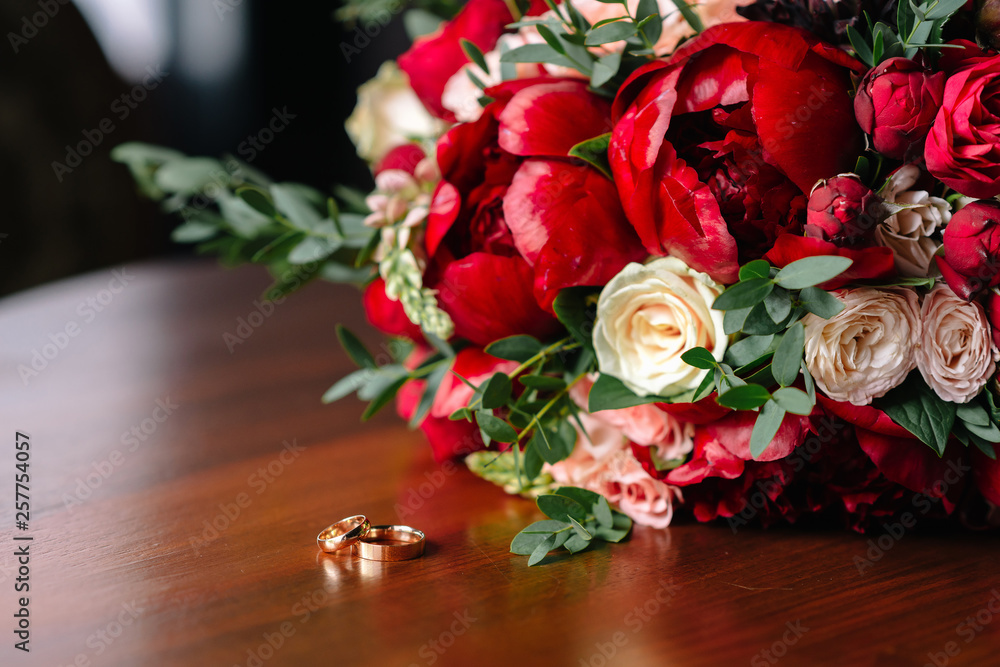 Obraz premium the bride's bouquet of red roses and wedding rings are on the table