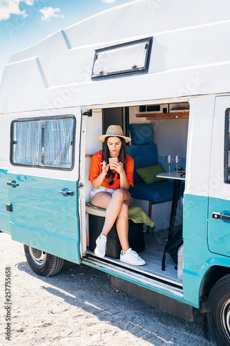 Young woman sitting in her camper van smoking and using smartphone