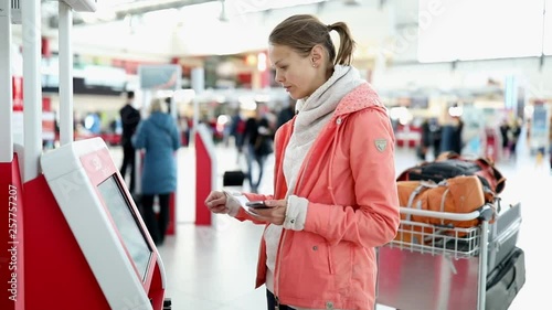 Young female traveller at the self check-in station at the airport, printing herself a boarding pass