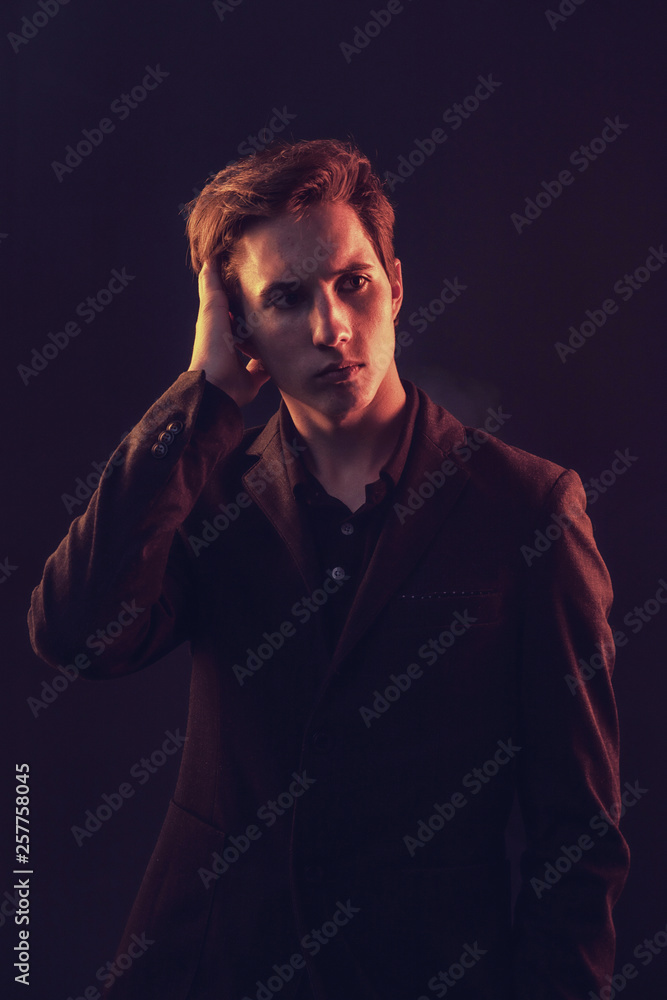Portrait of an expressive, stylish, young man in a strict suit in orange tones with a smoky background Portrait of an expressive, stylish, young man in a strict suit in orange tones with a smoky background
