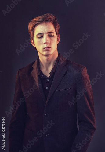 Portrait of an expressive, stylish, young man in a strict suit in orange tones with a smoky background