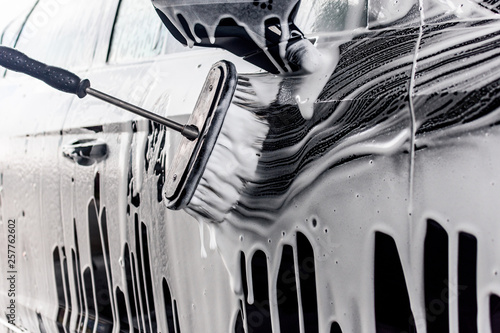 professionelle Autowäsche in einer Waschstraße- Mann reinigt den lack eines Fahrzeuges mit wasser und schaum_ professional car wash in a car wash man cleans the paint of a vehicle with water and foam photo