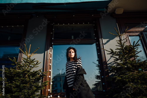 beautiful young brunette girl in black coat walking along city street, woman is relaxing outdoors © Pavel