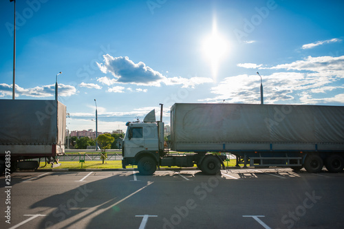 A white semi truck with a cargo trailer rides into the parking lot and parked with other vehicles. Wagons on unloading goods. photo