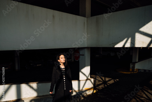 beautiful young happy girl in black pants and striped vest on parking lot, brunette woman is resting outdoors