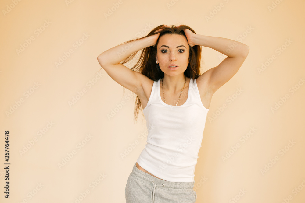 a young girl in a white T-shirt on a uniform beige background makes an emotion of happiness, rejoices, smiles, shows lashes a young girl in a white T-shirt on a uniform beige background makes an emotion of happiness, rejoices, smiles, shows lashes