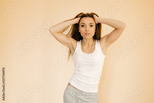 a young girl in a white T-shirt on a uniform beige background makes an emotion of happiness, rejoices, smiles, shows lashes