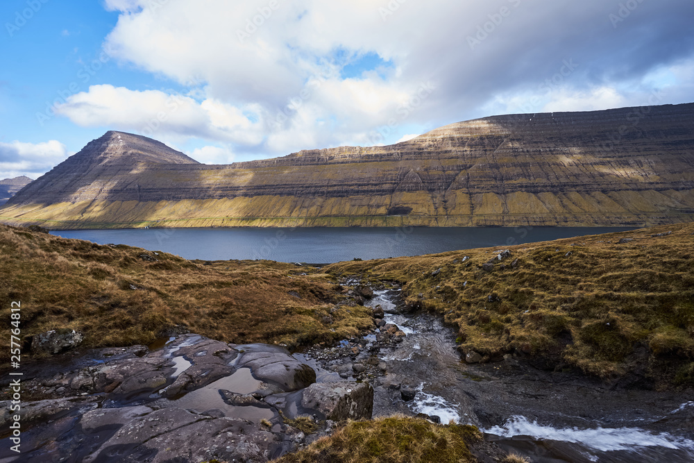 Beautiful landscape Picture of large fjord and small water creek with water from melting snow on the Faroese island Bordoy in the spring sunny day. Faroe islands show wild scandinavian countryside. 